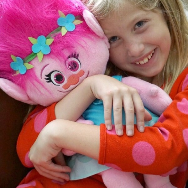 A smiling girl hugs a large pink doll with blue flower hair accessories, both dressed in colorful outfits—perfectly illustrating great presents for girls.