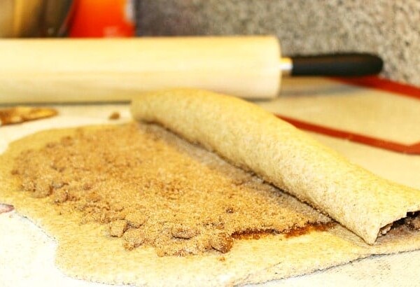 A delicious dough is being skillfully rolled with cinnamon and sugar, hinting at the creation of irresistible gingerbread cinnamon rolls, with a trusty rolling pin in the background.