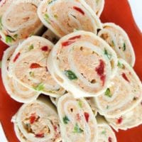 A vibrant orange dish showcases a plate of cream cheese pinwheels, bursting with the colorful crunch of red and green bell peppers.