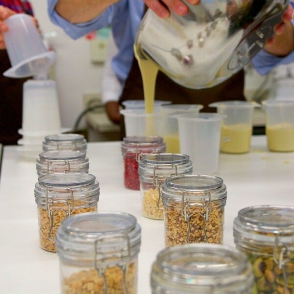 A person is skillfully pouring a simple and delicious liquid into jars filled with an array of dry ingredients on the table, creating a scene reminiscent of crafting a homemade treat as delightful as Hershey's milk chocolate.