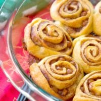 Crescent roll cinnamon rolls sit elegantly in a glass dish atop a vibrant red tablecloth.