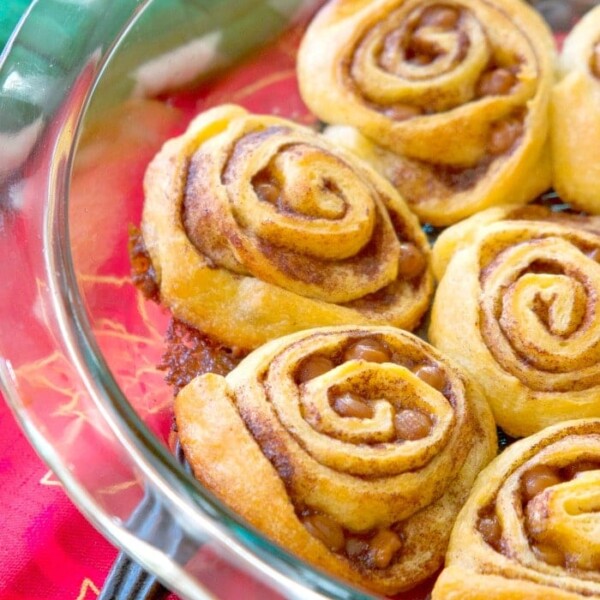 Crescent roll cinnamon rolls sit elegantly in a glass dish atop a vibrant red tablecloth.