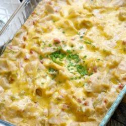 A cheesy chicken tortilla bake topped with chopped green herbs in a glass baking dish.