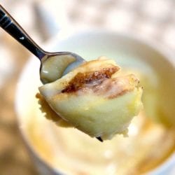 Close-up of a spoon holding a piece of cinnamon roll above a mug.