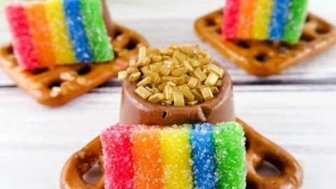 Pretzel squares topped with chocolate, gold sprinkles, and rainbow candy strips make the perfect St. Patrick's Day treats on a wooden surface.
