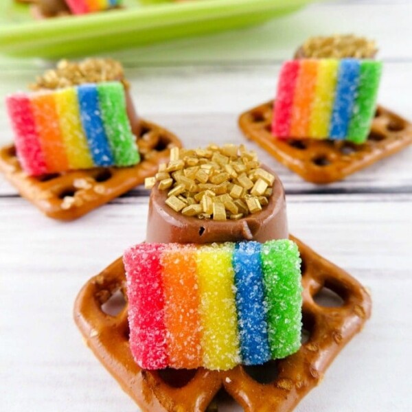 Pretzel squares topped with chocolate, gold sprinkles, and rainbow candy strips make the perfect St. Patrick's Day treats on a wooden surface.