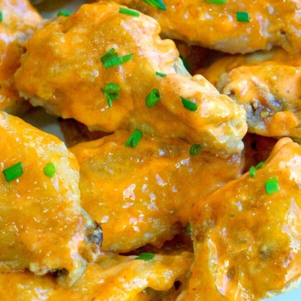 Close-up of glazed sriracha chicken wings garnished with chopped chives.