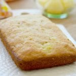 Freshly baked pineapple bread loaf on a white plate, reminiscent of delicious banana pineapple muffins, with a bowl of pineapple chunks in the background.