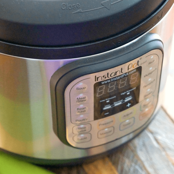 A close-up of an Instant Pot electric pressure cooker showcases its control panel, featuring buttons for settings like Soup, Meat/Stew, and Bean/Chili. The lid is partially visible as the appliance rests on a wooden surface, ready to bring cookbook recipes to life with ease.