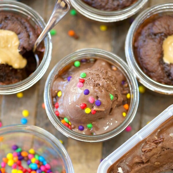 Copycat wicked good cupcakes feature chocolate desserts layered with peanut butter, multicolored sprinkles, and ice cream in glass jars on a rustic wooden table.