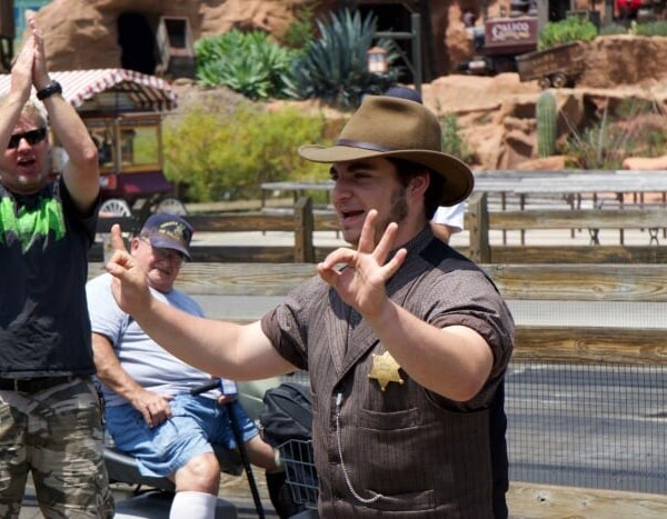 At Knott's Berry Farm, a man in a cowboy hat joyfully interacts with the crowd during the Ghost Town Alive event, with people clapping and smiling in the background.