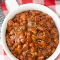 A bowl of no soak Instant Pot baked beans rests on a red and white checkered tablecloth.