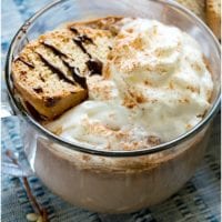 A cup of hot chocolate made from scratch, topped with whipped cream and served alongside biscotti on a blue textured cloth.