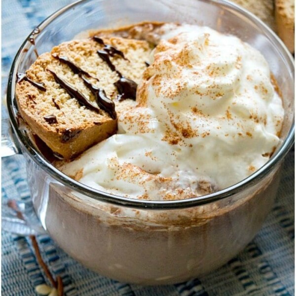 A cup of hot chocolate made from scratch, topped with whipped cream and served alongside biscotti on a blue textured cloth.