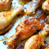 Close-up of teriyaki chicken drumsticks glazed with a sticky sauce, arranged on a baking tray. The drumsticks boast a golden-brown, crispy exterior with visible sesame seeds and caramelized edges.