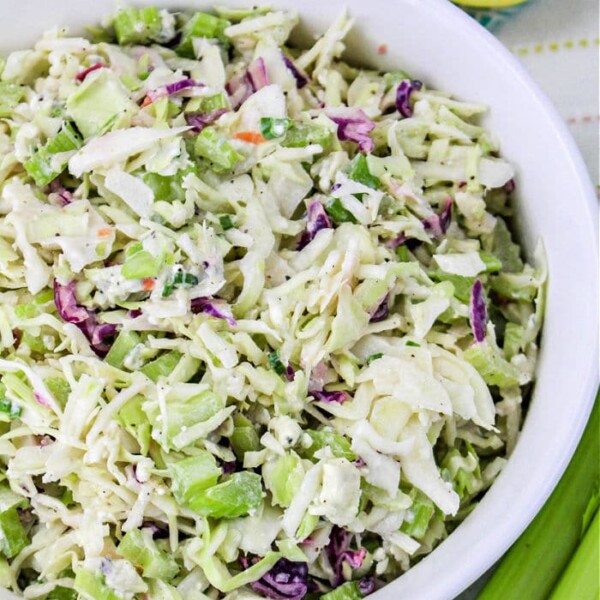 A bowl of fresh coleslaw, perfect for a pulled pork feast, features crisp cabbage, carrots, and green onions, all served beside sliced lemons.