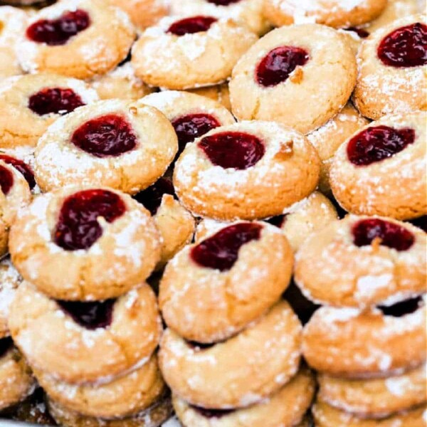 A delightful pile of thumbprint cookies filled with rich red jam resembles the classic joy of peanut butter and grape jelly cookies, all dusted with a light sprinkle of powdered sugar.