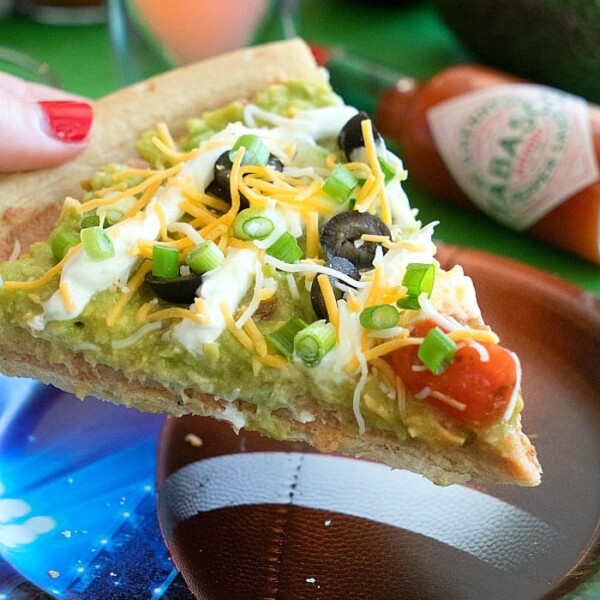 The 7 layer dip pizza features a slice topped with guacamole, cheese, olives, and tomatoes served stylishly on a football-themed plate.