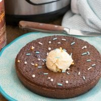 Instant pot chocolate pudding cake topped with sprinkles and ice cream, served on a blue plate near a pressure cooker.