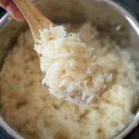 A wooden spoon holds perfectly cooked white rice over an open instant pot, showcasing a seamless blend of tradition and modern convenience.