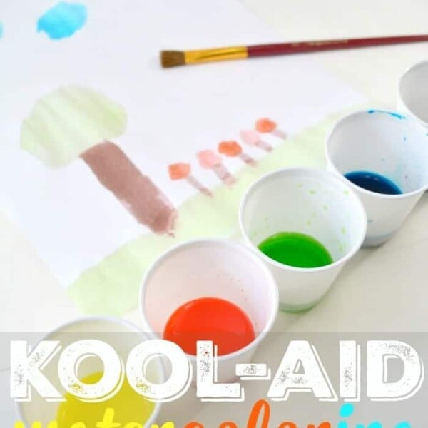 Watercolor painting with trees and sky using vibrant Kool-Aid paint; five cups filled with different colors and a brush are visible.