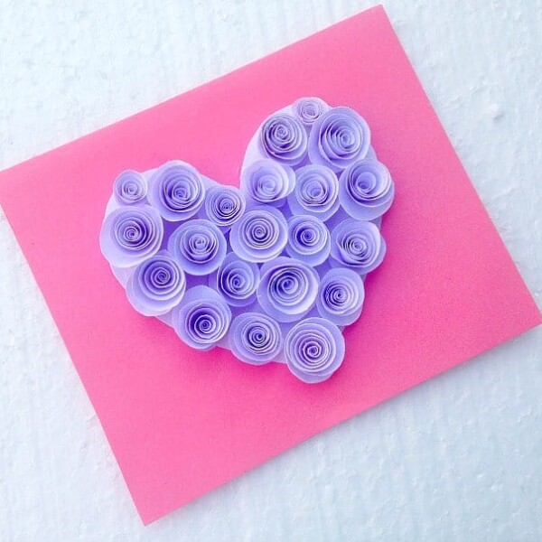 A charming pop-up heart card featuring a purple paper rosette adorns a pink backdrop, set against a textured white background.