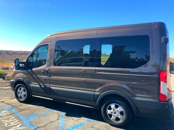 A brown passenger van, ideal for a road trip blog, is parked in a sunny outdoor area with a blue sky as the backdrop.