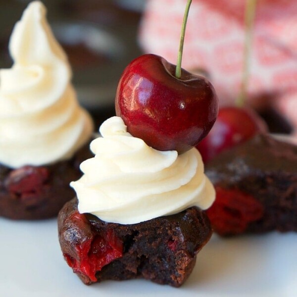 Indulge in this chocolate cherry brownie with white frosting, crowned by a fresh cherry, resting elegantly on a plate. Nearby, cherry brownies make a tempting appearance, offering a glimpse of their rich, chocolatey texture interspersed with luscious cherries.