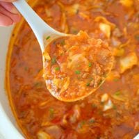 A ladle holds a portion of hearty slow cooker stuffed cabbage soup over a pot, showcasing chunks of cabbage, ground meat, and a rich tomato-based broth.