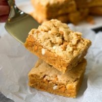 A hand holds a metal spatula, expertly lifting two stacked decadent peanut butter cookie brownies.