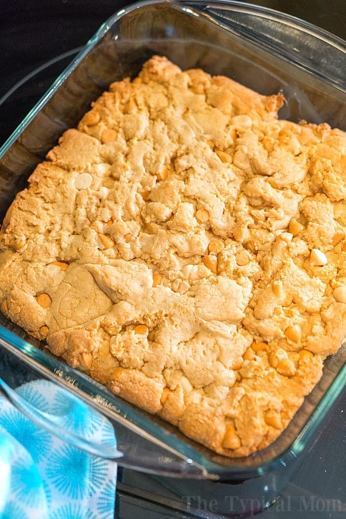 Baked dessert with a golden crust, featuring white chips and a hint of peanut butter cookie richness, in a square glass dish on a blue-patterned surface.