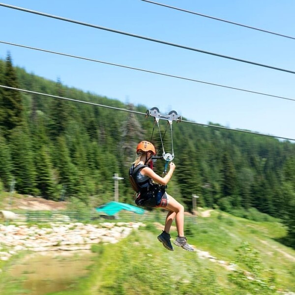 Person ziplining over a lush, green landscape at Schweitzer Resort, with Schweitzer Summer Activities text at the top.