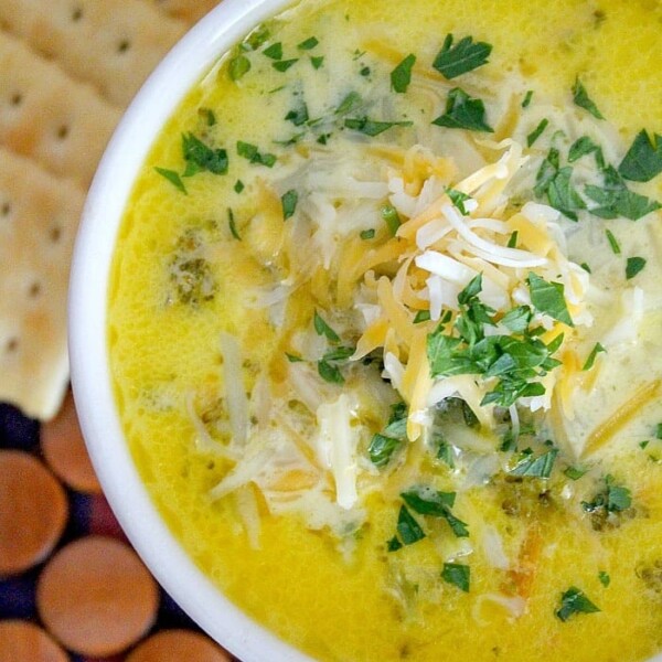 A bowl of Pressure Cooker Broccoli Cheese Soup topped with shredded cheese and parsley, served with crackers.