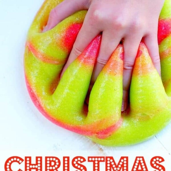 A hand presses into a swirl of brightly colored red and green Christmas slime with a glossy texture. The words Christmas Slime are displayed in festive letters at the bottom of the image.