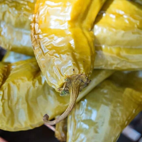 Close-up of roasted chiles with wrinkled skin and stems, arranged alongside smoked chiles on a grill.