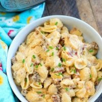 A bowl of creamy pasta shells with ground meat and melted cheese, perfect for meat lovers, garnished with chopped chives. A colorful towel is on the side. An Instant Pot stands proudly in the background on a wooden surface, hinting at this pressure cooker mac and cheese's delicious origin.