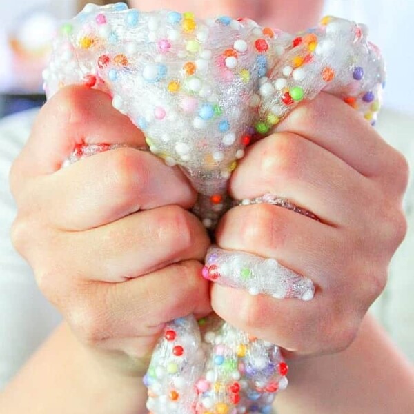 Person squeezing vibrant, beaded slime with both hands, enjoying the fun and creativity of crafting slime without borax.