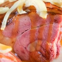 Close-up of glazed ham topped with sliced onions, reminiscent of a hearty Dutch oven ham.