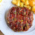 Pressure cooker meatloaf with herbs is elegantly glazed and served on a white plate, paired with perfectly roasted potato cubes.