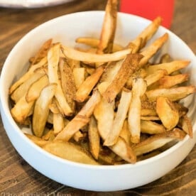 A bowl of golden-brown homemade French fries, perfectly crisped using the Ninja Foodi, sits invitingly on a wooden table.