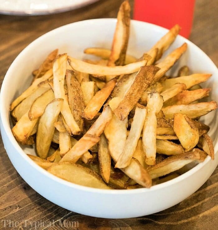 A bowl of golden-brown homemade French fries, perfectly crisped using the Ninja Foodi, sits invitingly on a wooden table.