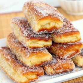 A stack of sugar-coated, flaky pastry sticks on a white plate offers a delightful crunch reminiscent of peanut butter and jelly donuts.