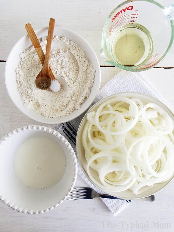 Air fried crispy fried onions can be deep fried in oil or you can make air fryer onion rings too! Want homemade French's fried onions, they're way better than canned! #friedonions #onions #airfryer #onionrings #frenchsfriedonions Bowl of flour, milk, crispy fried onions, and oil with utensils on a white surface.