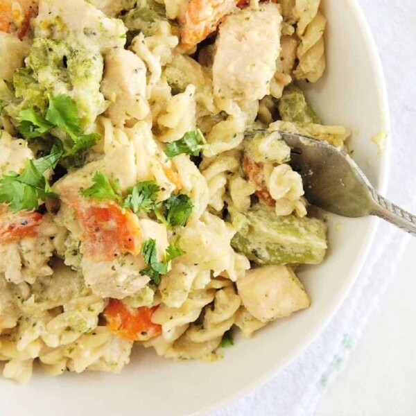 A bowl of creamy Instant Pot chicken pasta with chunks of broccoli and carrots, garnished with cilantro. A fork is placed on the edge of the bowl.