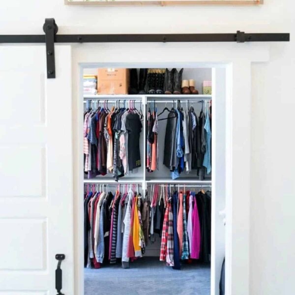 View of a neatly organized closet, showcasing hanging clothes and shelves, seamlessly created by turning a bedroom into this elegant space, all visible through a sliding door.