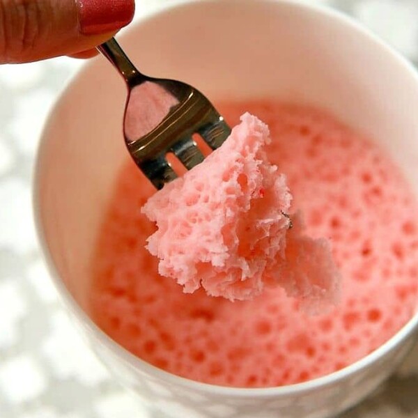 A fork holding a piece of fluffy strawberry cake from a white mug.