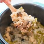 A hand gracefully serves a delightful instant pot cream of mushroom rice dish from a pot with a wooden spoon.