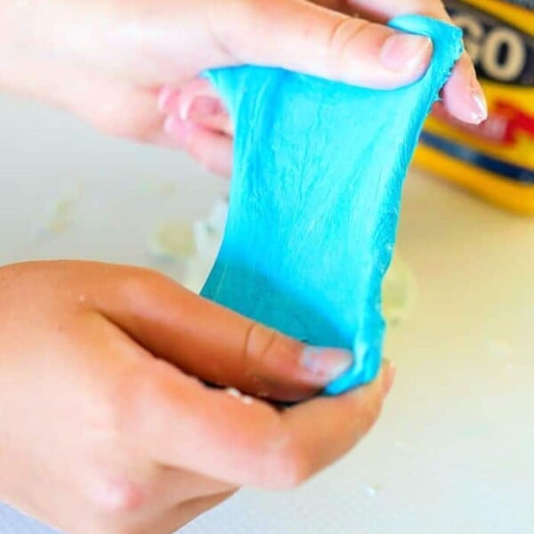 Hands stretching blue slime with a box labeled Argo in the background, showcasing a creative twist on how to make slime without glue.