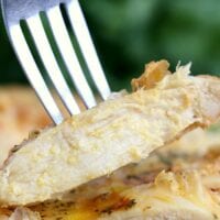 A fork holds a cooked chicken breast slice, showcasing its tender and juicy interior achieved by cooking a frozen chicken breast in an air fryer. The meat is seasoned with herbs and spices, while the background blurs into soothing shades of green.