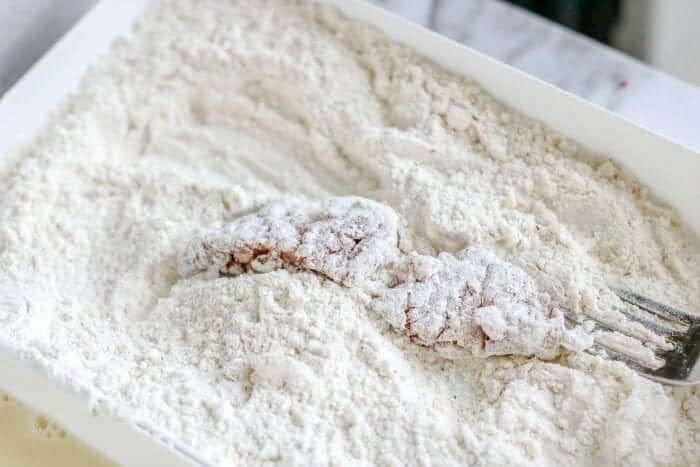 A piece of meat for air fryer chicken fried steak is being coated in flour with a fork in a white dish.